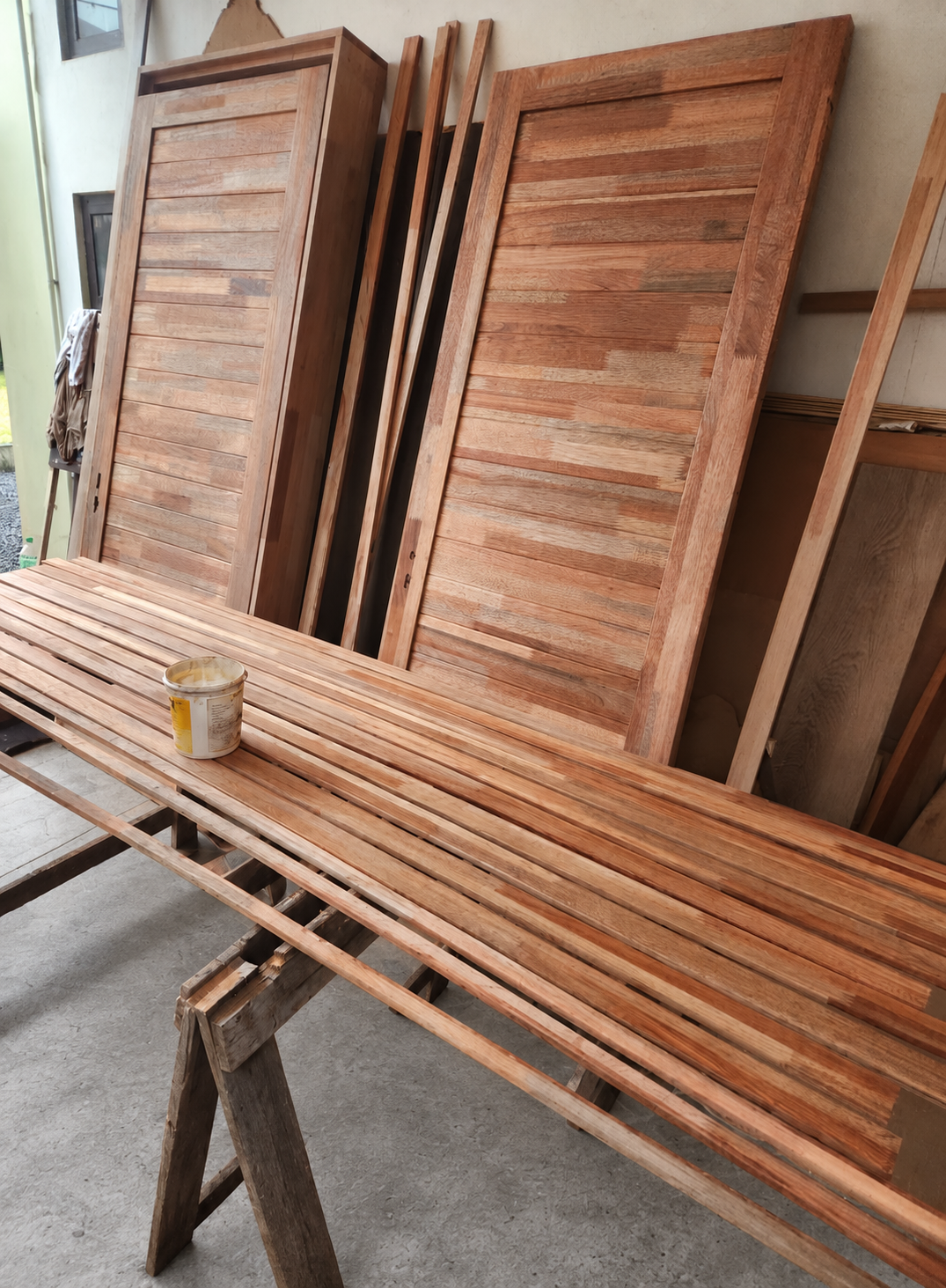 Timber doors behind a long slatted workpiece resting on trestles in a workshop