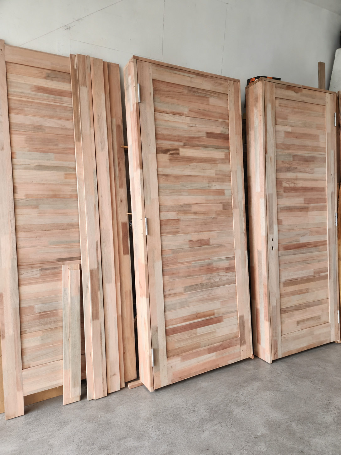 Unfinished timber doors and timber boards standing together on a gray workshop floor