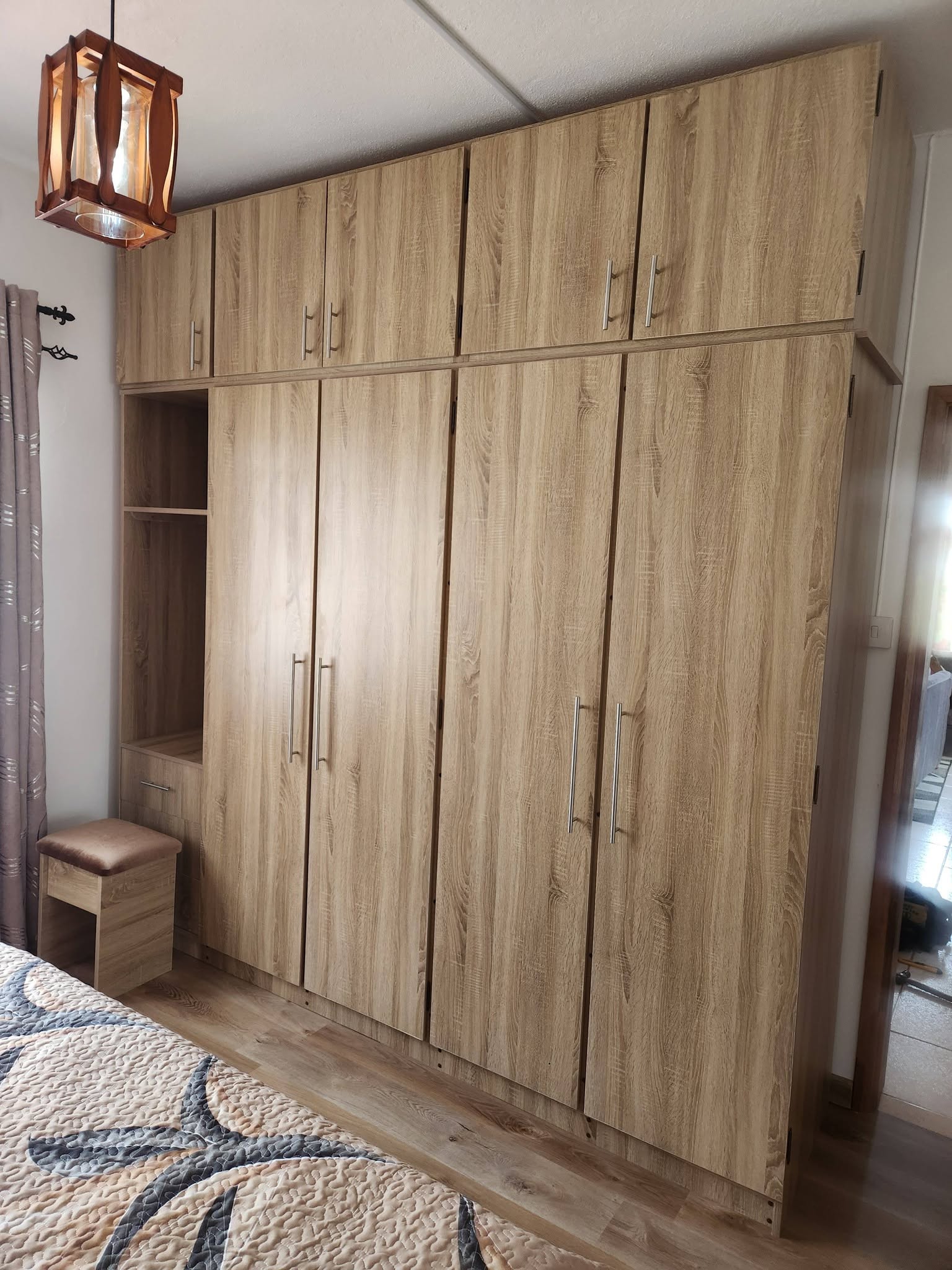 Light wood fitted bedroom wardrobes with upper cabinets, an open niche and silver handles