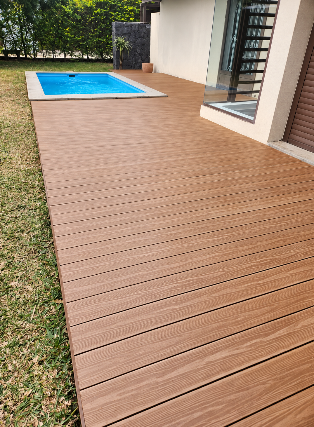 Grooved decking around a swimming pool beside a house and garden